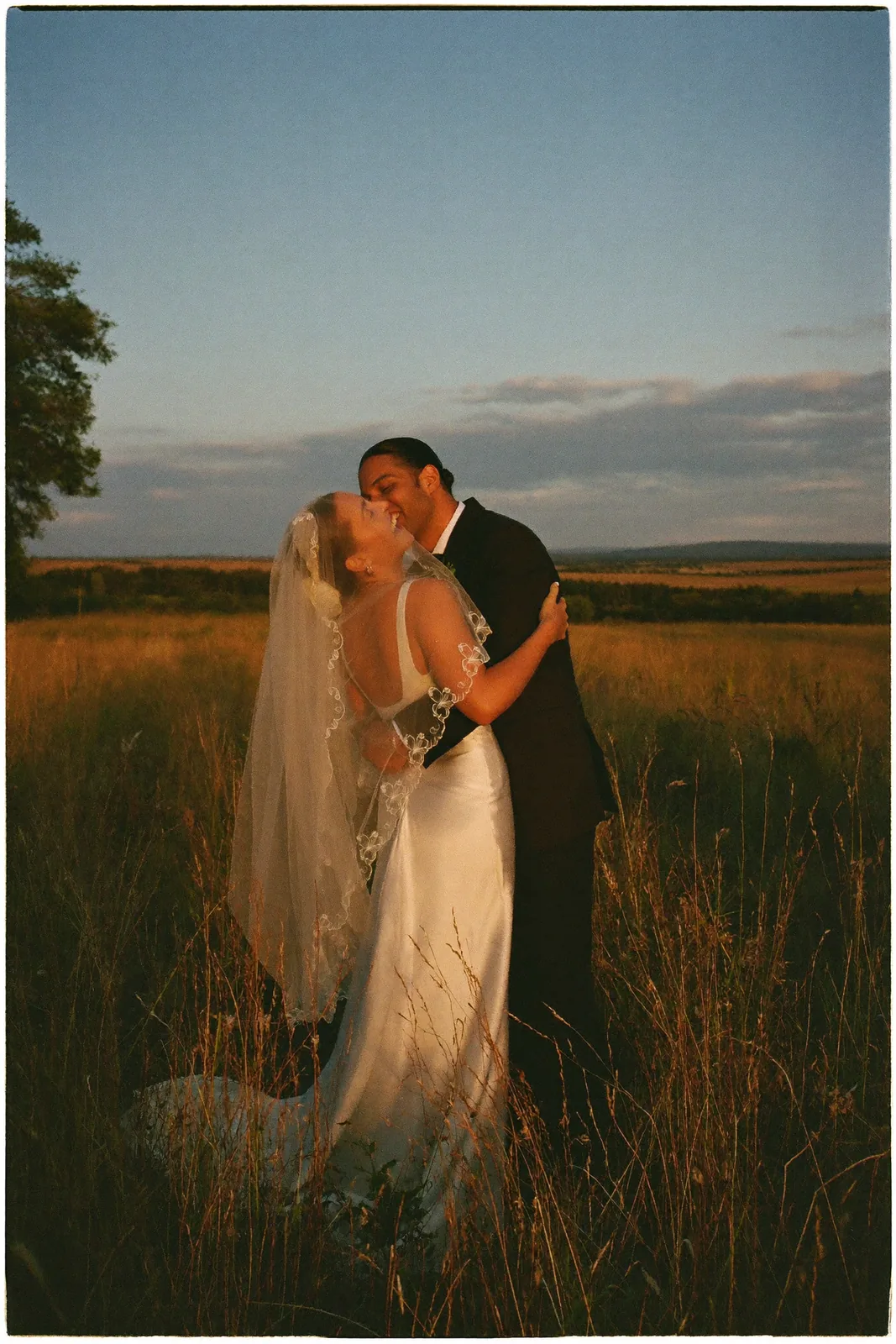 Smiling newlyweds hugging in a meadow at sunset